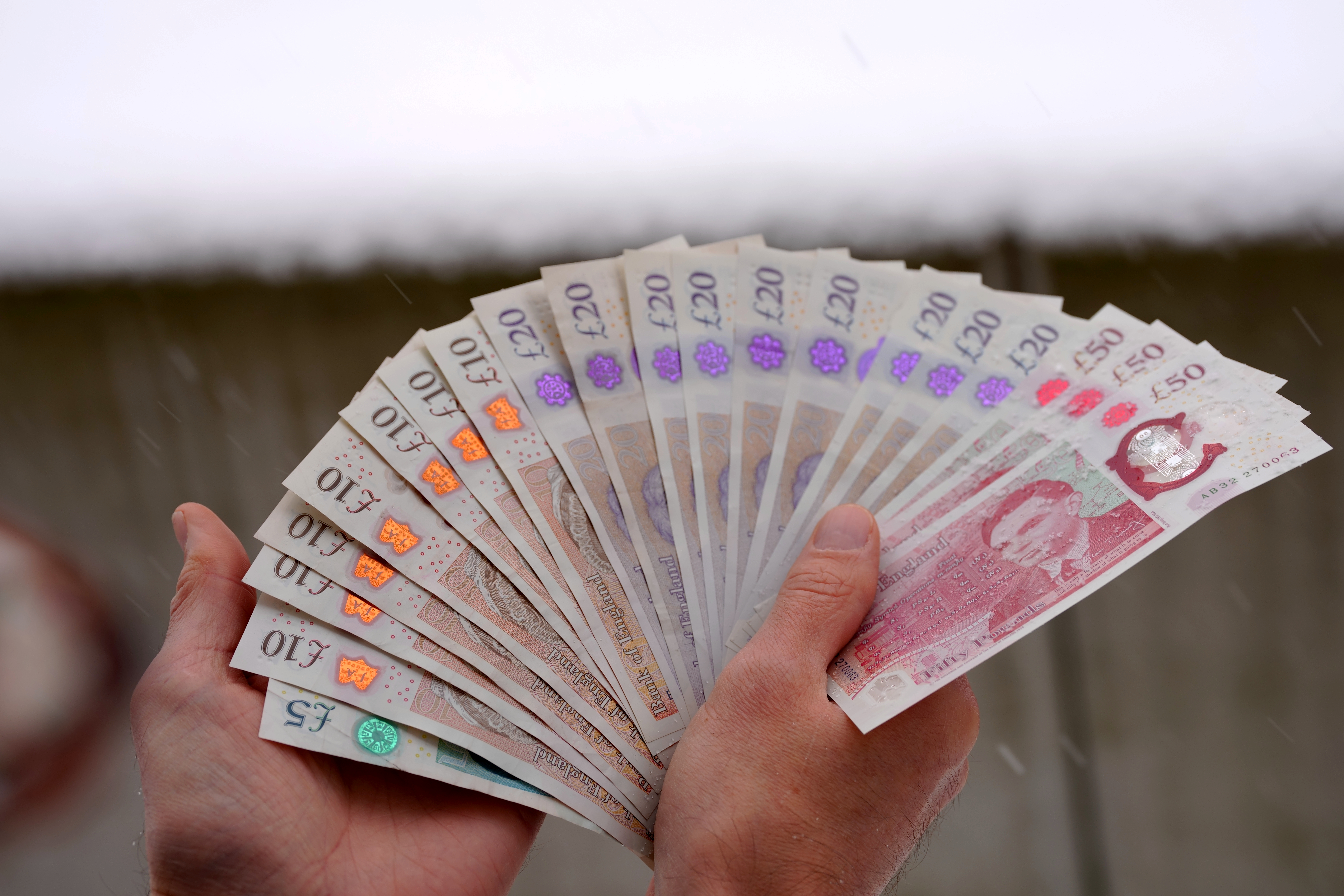 Close-up of man holding fan of English Pound banknotes outdoors at terrace on a snowy winter day. Photo taken January 8th, 2026, Zurich, Switzerland.